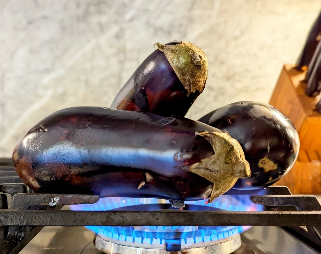 eggplants roasting over gas stove flame