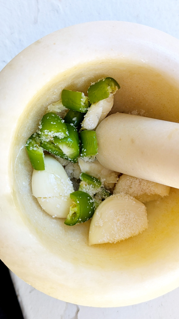 Pound garlic, chili pepper, and salt in mortar and pestle